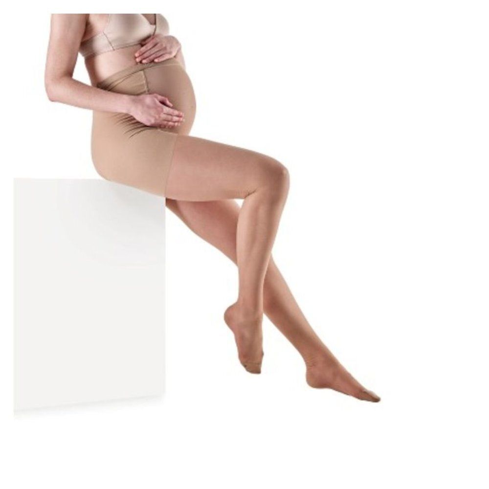 Femme enceinte assise. Porte un collant. Vêtement couleur chair. Fond blanc.