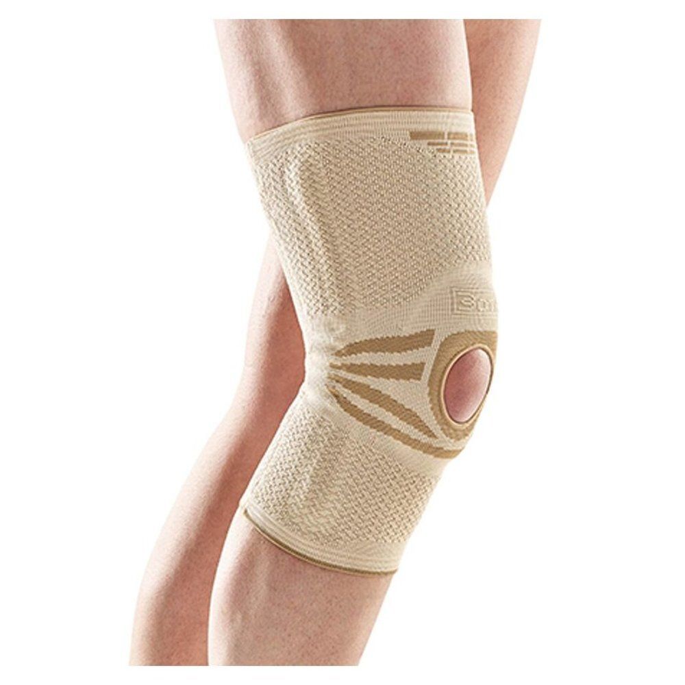 Orthèse de genou beige sur une jambe. Rotule ouverte. Matière élastique avec renforts.