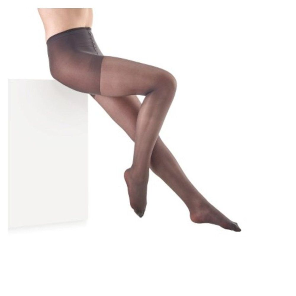 Collants gris foncé. Femme assise sur un bloc blanc. Vue des collants sur les jambes.