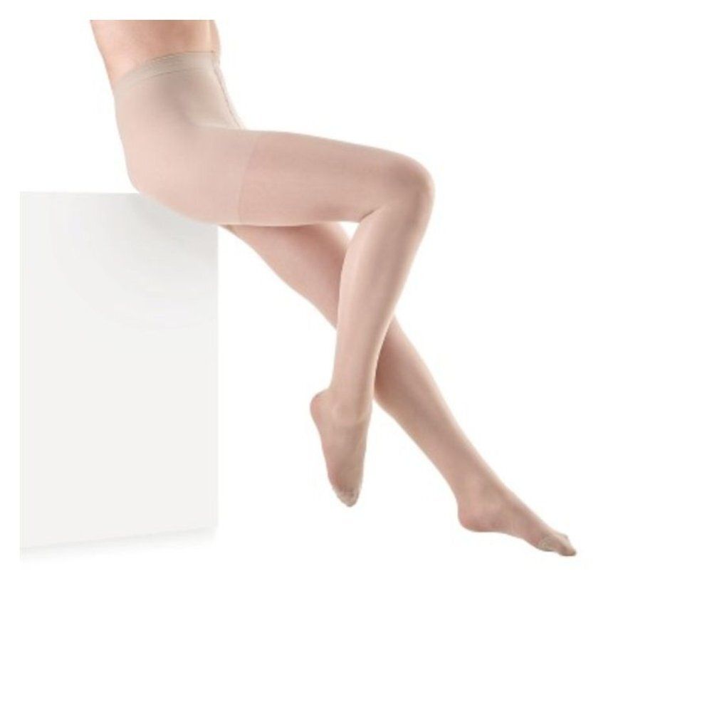 Collant couleur chair. Femme assise sur un cube blanc. Jambes et collant visibles.
