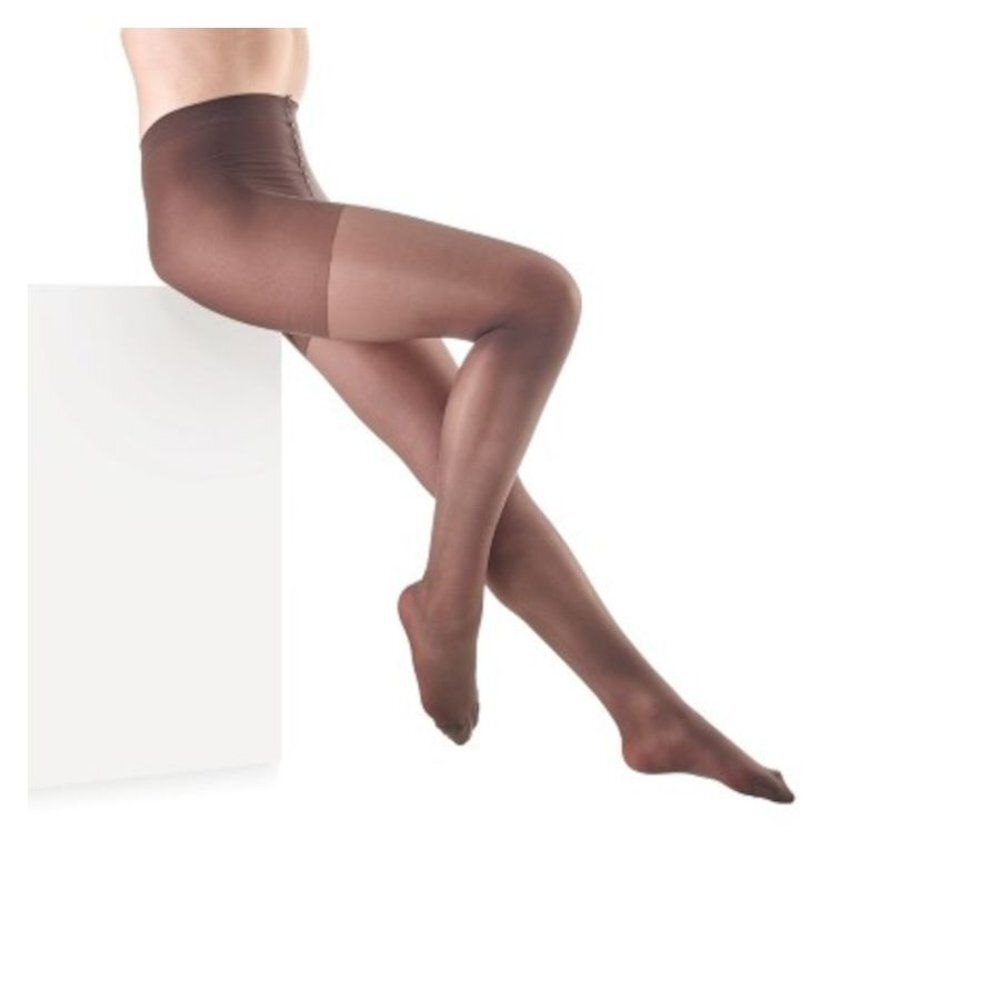 Collant marron. Vue rapprochée des jambes d'une personne assise sur un cube blanc.