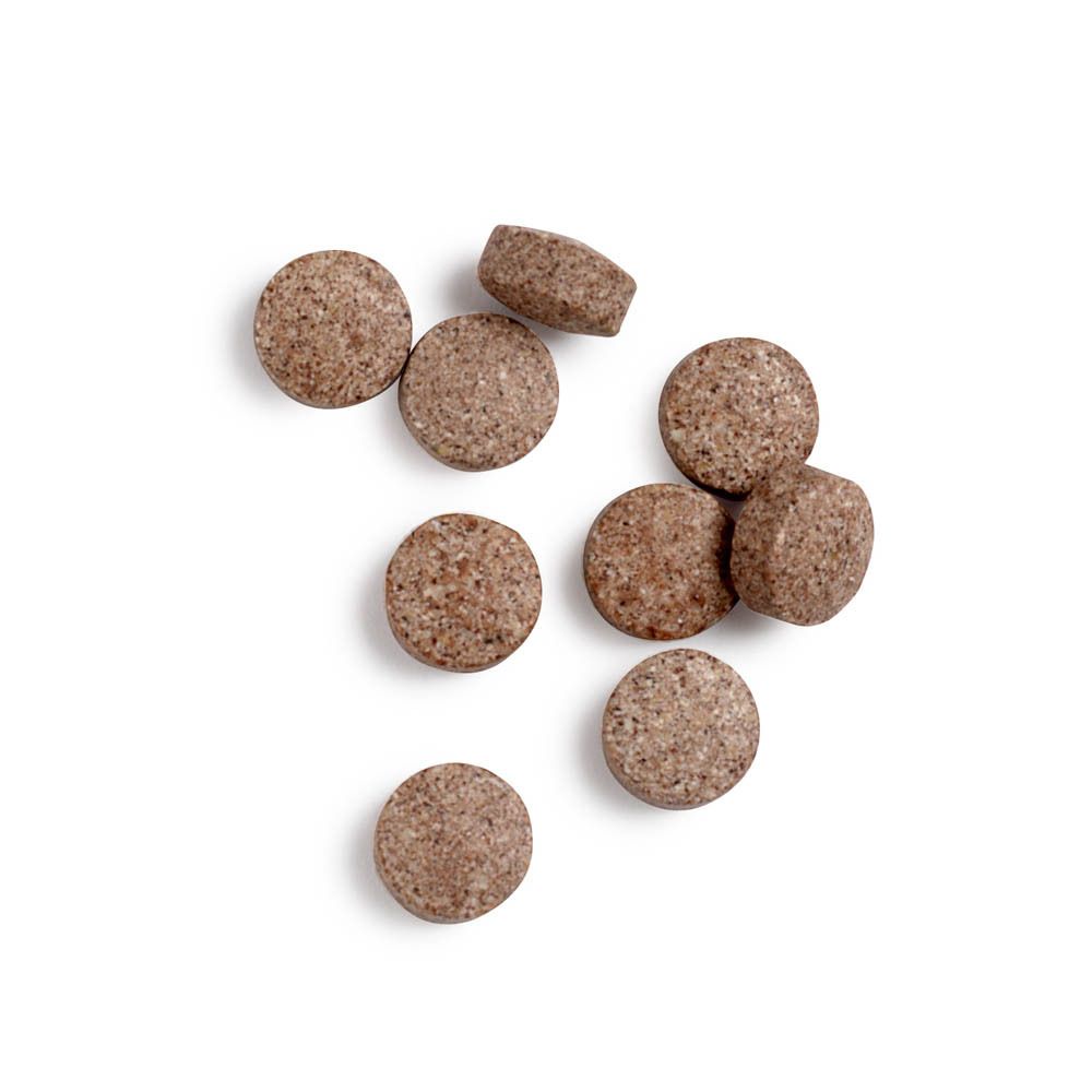 Ronde, bruine tabletten verspreid op witte achtergrond. Sommige tabletten hebben een onregelmatige vorm.