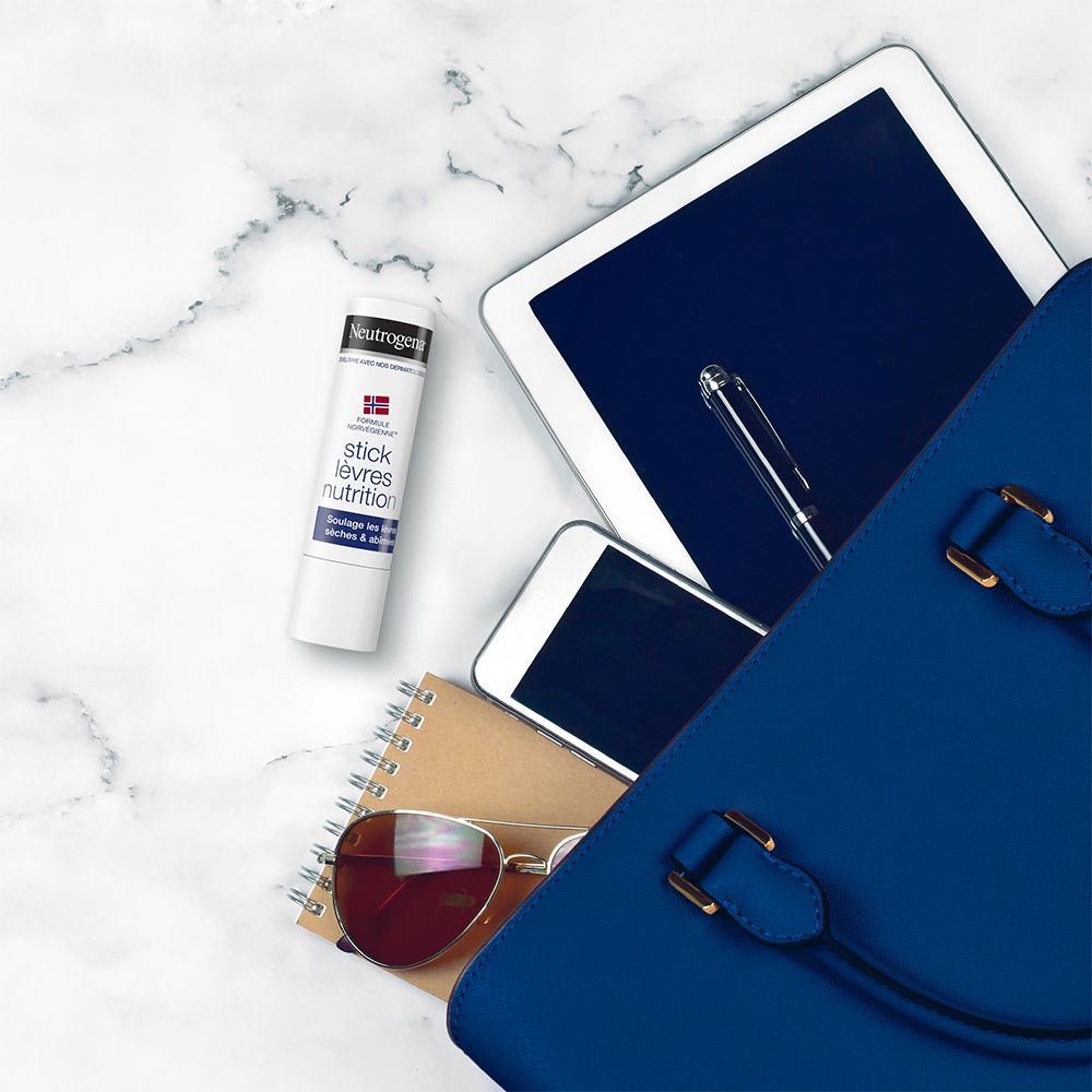 Stick lèvres Neutrogena dans sac à main bleu avec tablette, téléphone, stylo et lunettes de soleil.