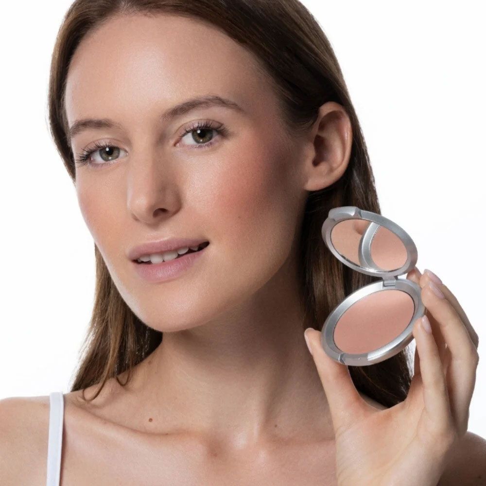 Femme tenant un blush en poudre. Boîtier argenté, poudre rose.