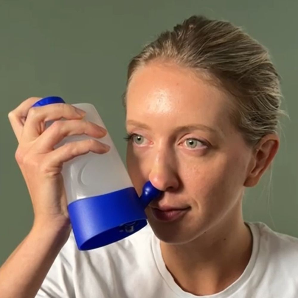 Close-up van een vrouw die een neusdouche gebruikt. Het product heeft een blauwe dop en basis.