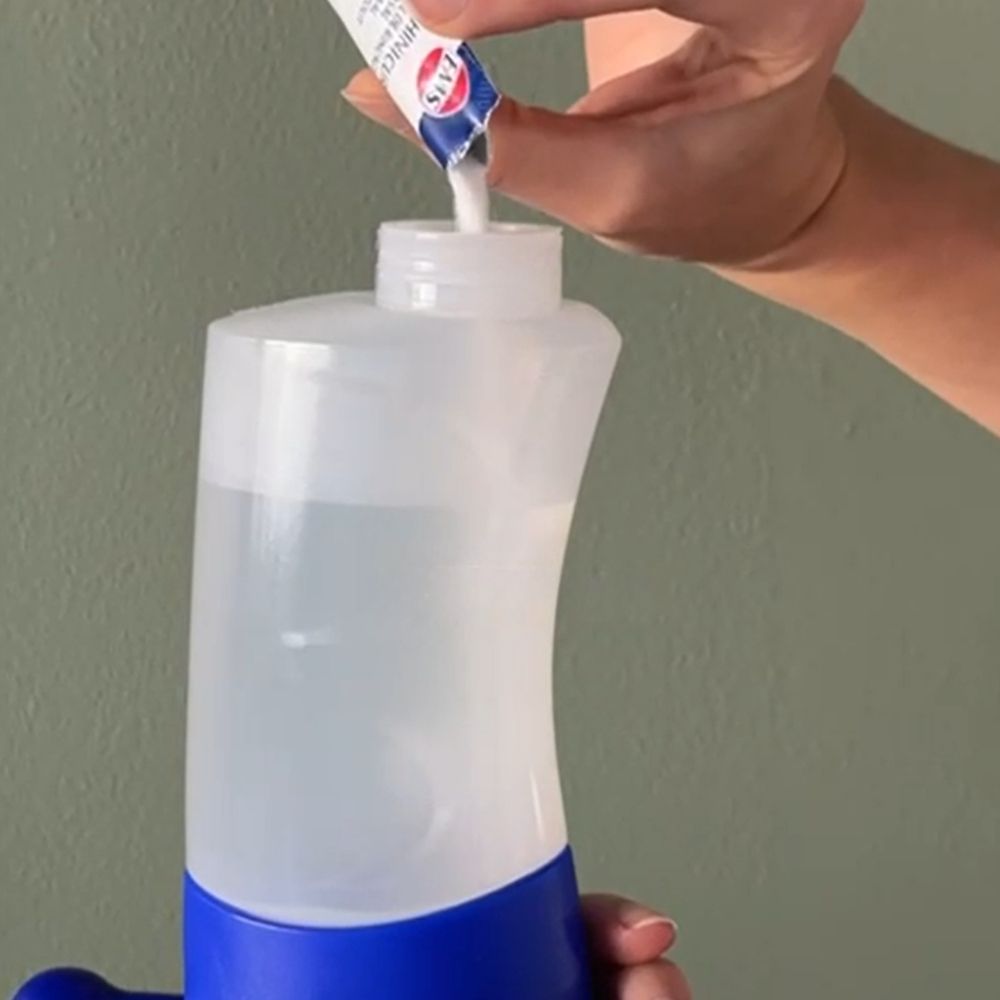 Personne verse de la poudre d'un sachet dans une bouteille de rinçage nasal. La bouteille est transparente avec une base bleue.