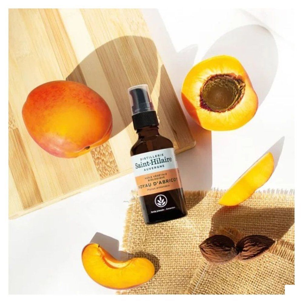 Fles met abrikozen en pitten op houten plank en linnen doek. Etiket met tekst: Huile Végétale Biologique, Noyau d'Abricot, Saint-Hilaire.