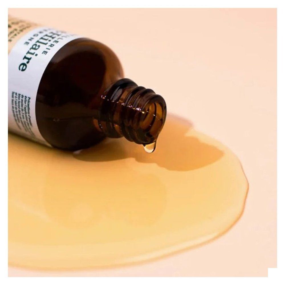 Flacon en verre brun, de l'huile coule sur une surface. Étiquette partiellement visible.