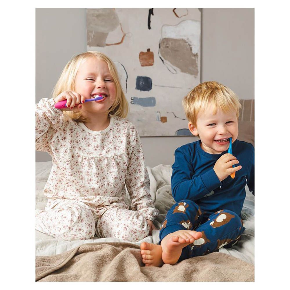 Twee kinderen poetsen hun tanden met tandenborstels. Zittend op een bed.