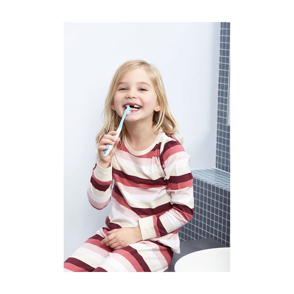 Une jeune fille se brosse les dents avec une brosse à dents bleue. Elle est assise sur un lavabo.