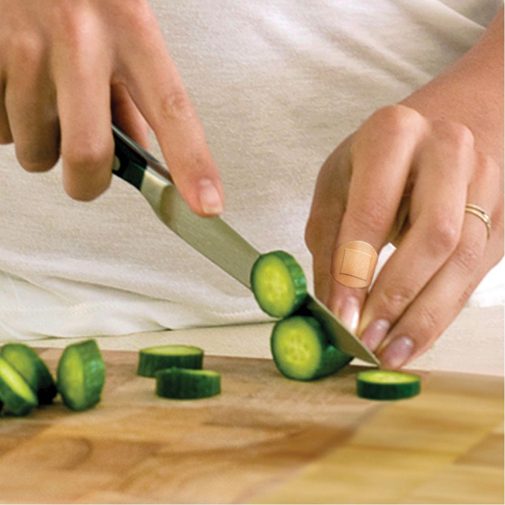 Personne coupant des concombres avec un couteau sur une planche à découper. Un pansement sur le doigt.