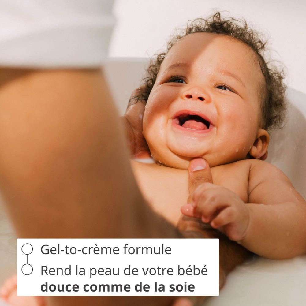 Des parents baignent un bébé dans une baignoire pour bébé, une bouteille Weleda Baby Calendula Cremebad à proximité.