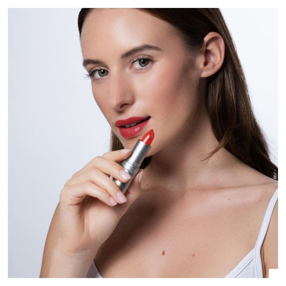 Femme tenant un rouge à lèvres argenté. Elle porte du rouge à lèvres rouge.