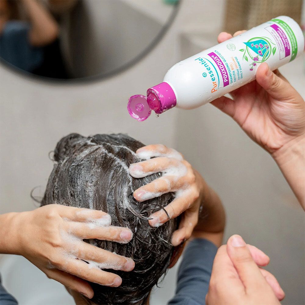 Personne se lave les cheveux avec du shampoing. Flacon bouchon violet. Inscription: Puressentiel Poudoux®.