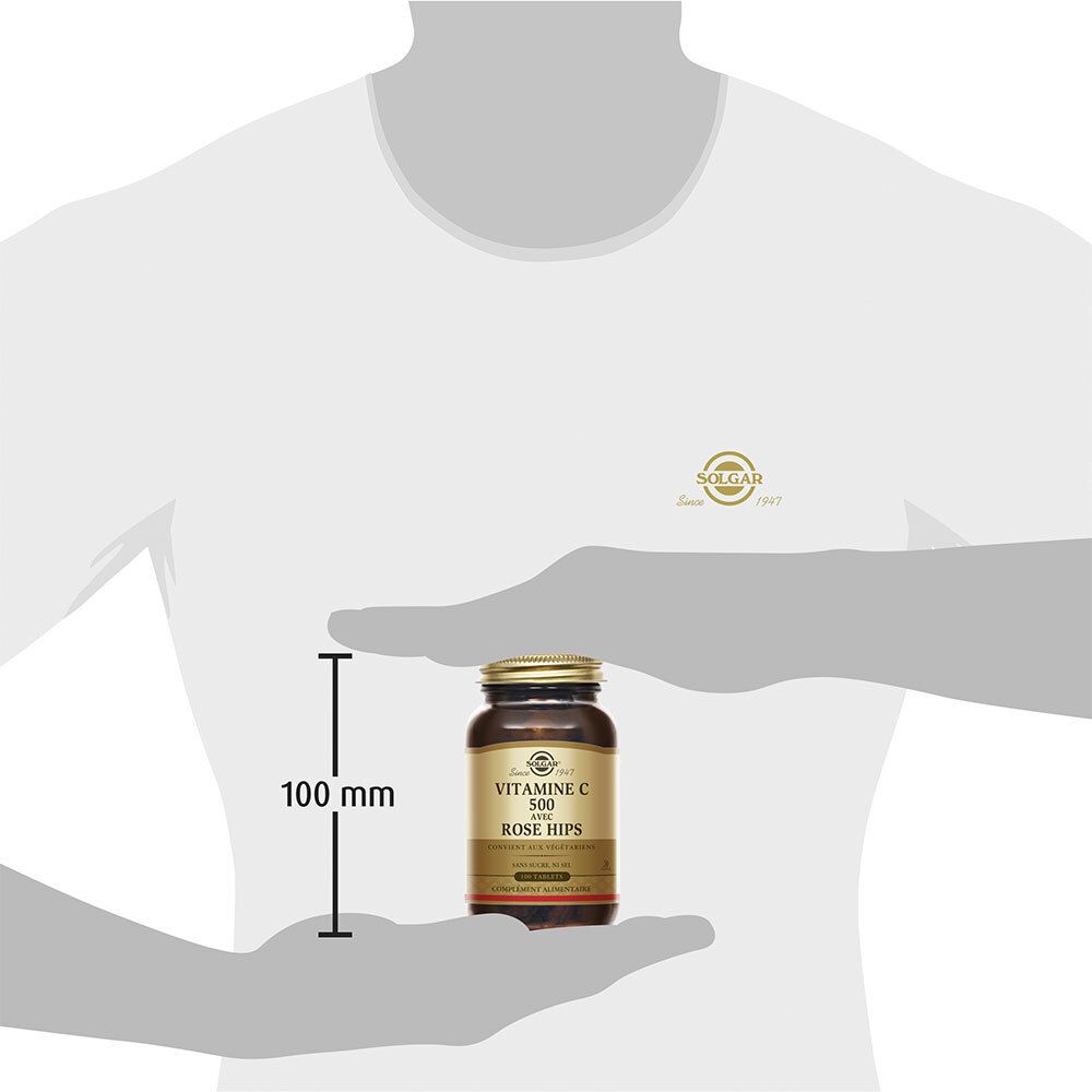 Persoon houdt een bruine glazen fles vast. De fles is 100 mm hoog. Op de fles staat: Vitamine C 500 met rozenbottel.