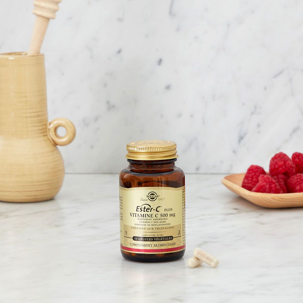 Glazen fles met vitamine C-capsules op marmer. Frambozen in een schaal.