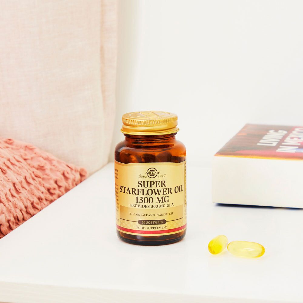 Bruine fles, gouden dop. Etiket: Solgar Super Starflower Oil 1300 mg, 30 softgels. Op tafel met kussen en boek.