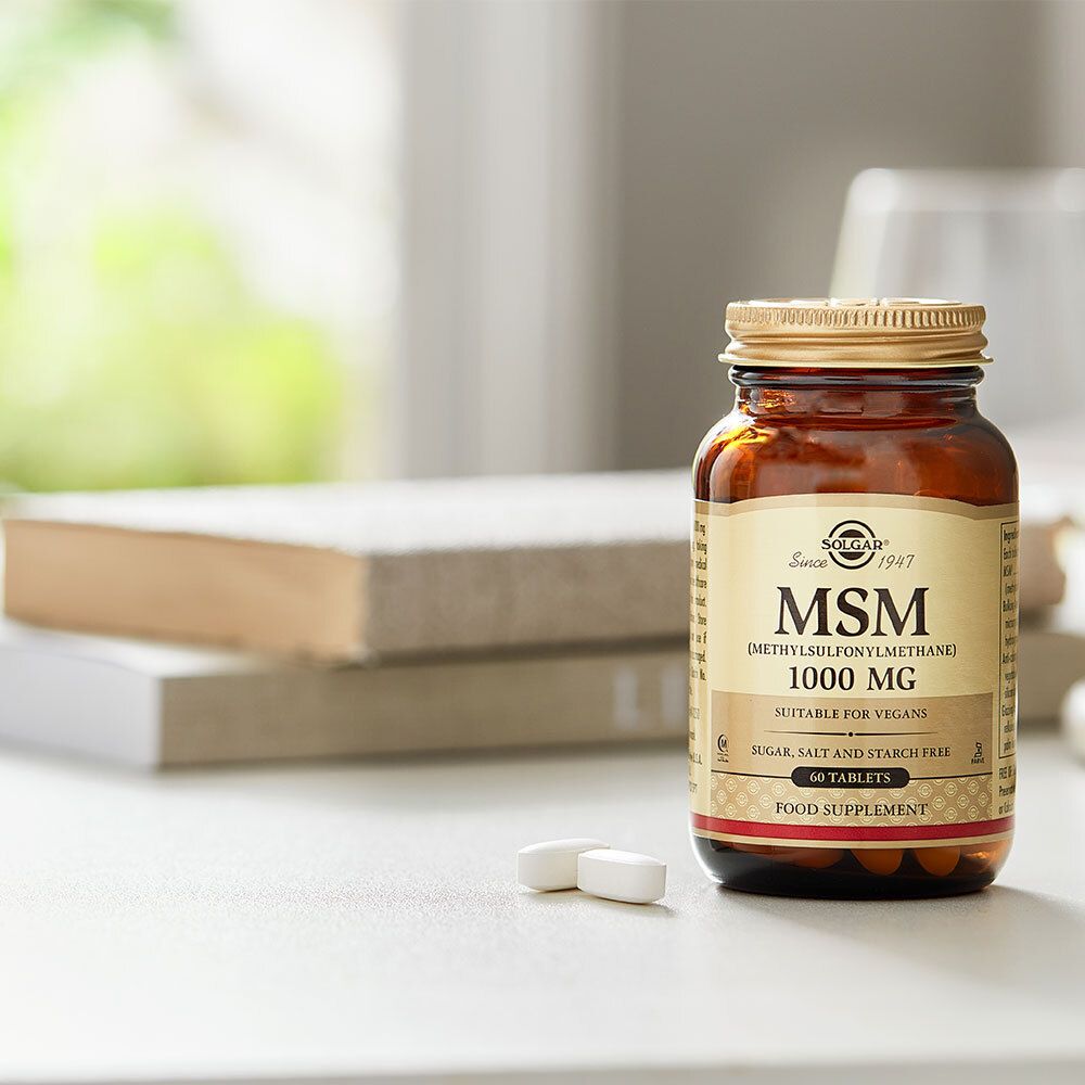 Fles MSM 1000 mg met tabletten op tafel. Merk Solgar, 60 tabletten. Achtergrond boeken.