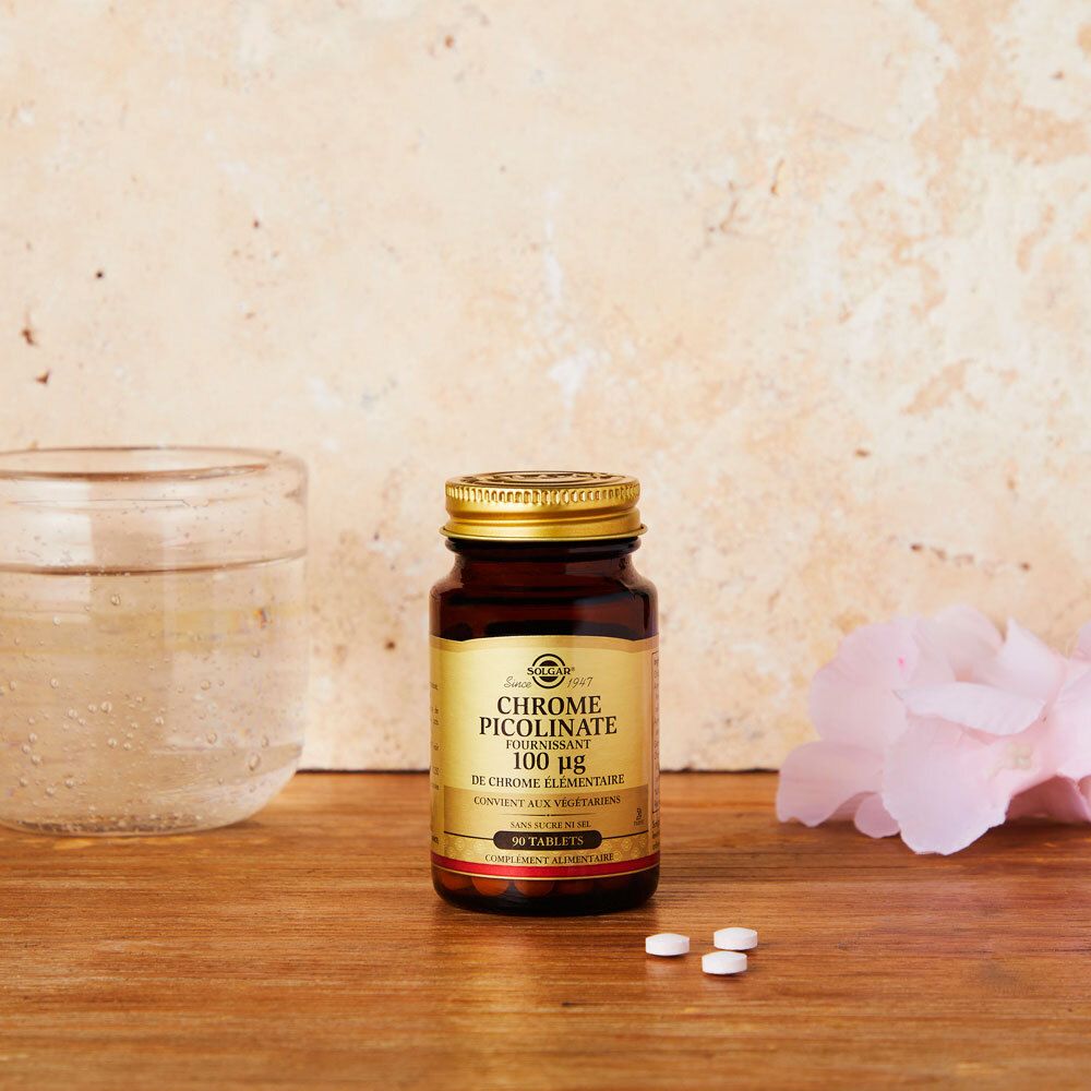 Bruine fles met tabletten op houten oppervlak. Glas water en bloem op de achtergrond.