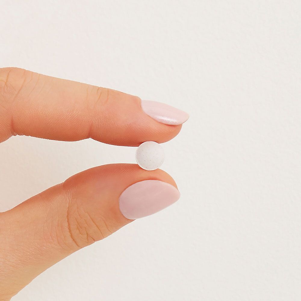 Een enkele, ronde, witte tablet, vastgehouden tussen vingers met roze nagellak.