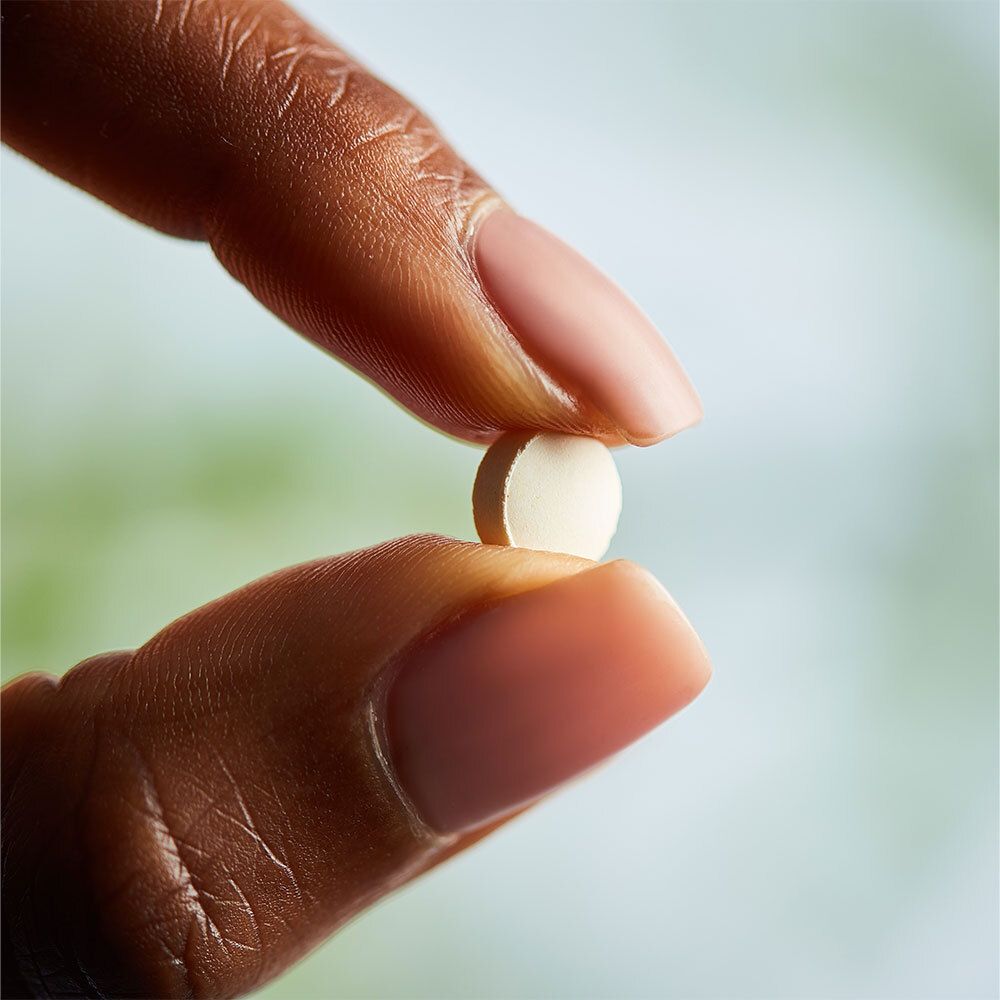 Hand die een enkele, ronde, witte tablet tussen de vingers houdt.