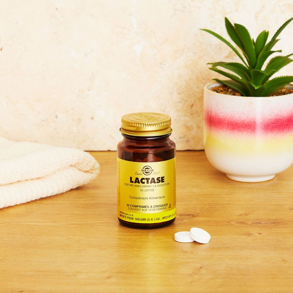 Flacon en verre brun avec couvercle doré et étiquette. Deux comprimés à côté. Fond : table et plante.