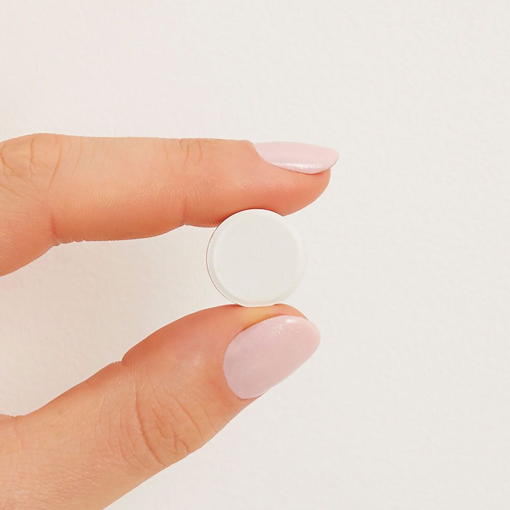 Un comprimé, blanc et rond, tenu par une main. Fond : blanc.