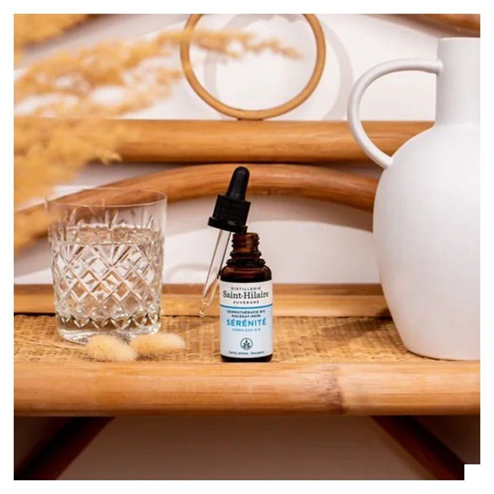 Flacon en verre brun avec compte-gouttes, verre d'eau, vase et décoration sur plateau.