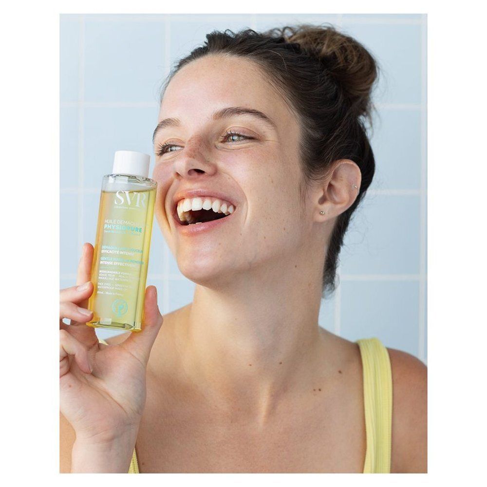 Femme tenant un flacon. Liquide jaune visible. Inscriptions SVR, PHYSIOPURE. Fond bleu. Femme souriante.