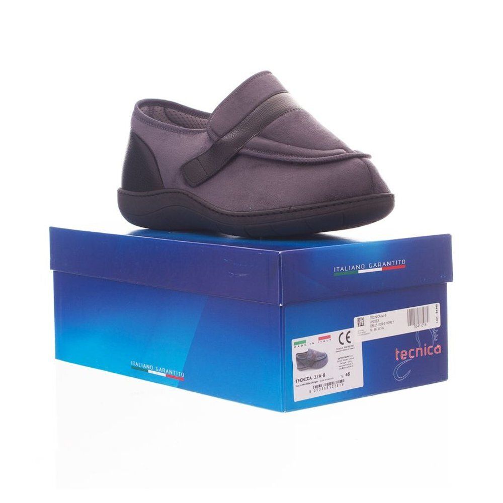 Slipper gris confort sur boîte bleue. Talon et bride noirs. Fermeture velcro. Semelle noire. Inscriptions sur la boîte.