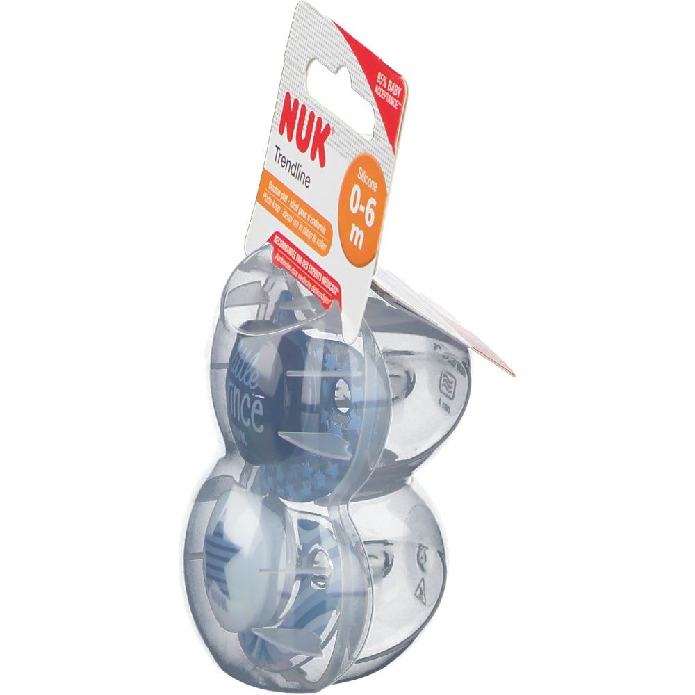 Deux sucettes bleues NUK Trendline dans un emballage. Visible : 'NUK Trendline', '0-6 m'. Emballage plastique.