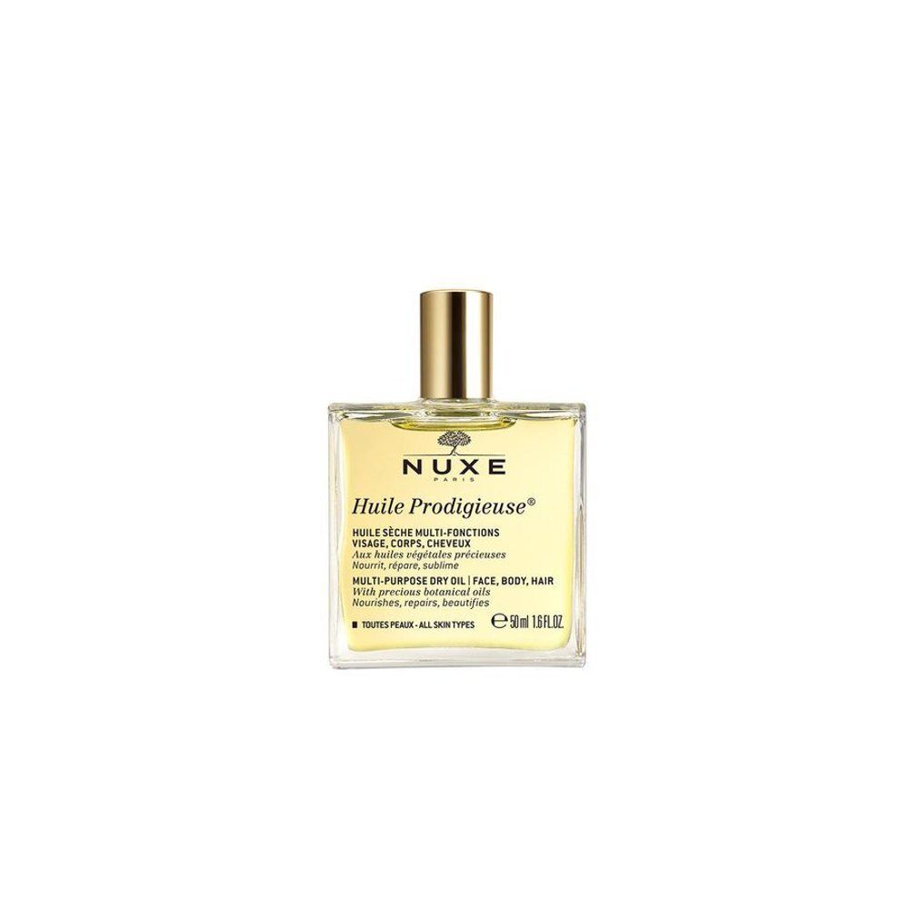 Nuxe Huile Prodigieuse droge olie fles op spiegelende ondergrond, omringd door witte bloemen.