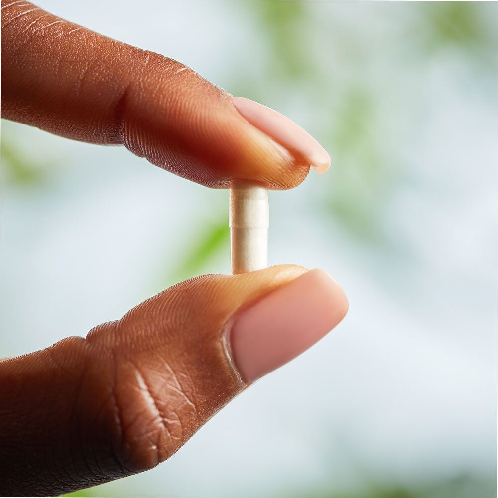 Een capsule tussen vingers. De capsule is wit en langwerpig.