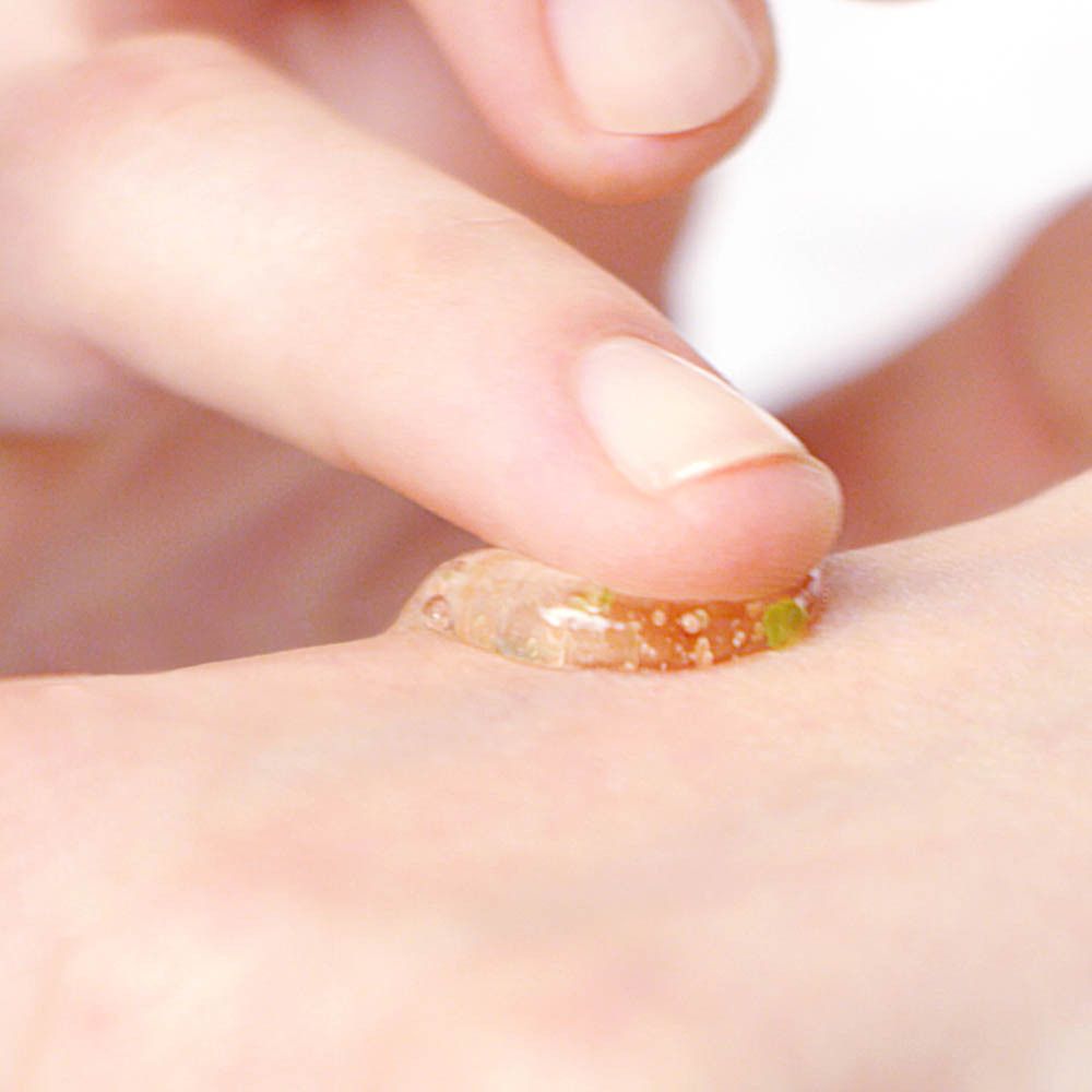 Le bout d'un doigt touche une goutte de gel transparent avec des particules vertes sur la peau.