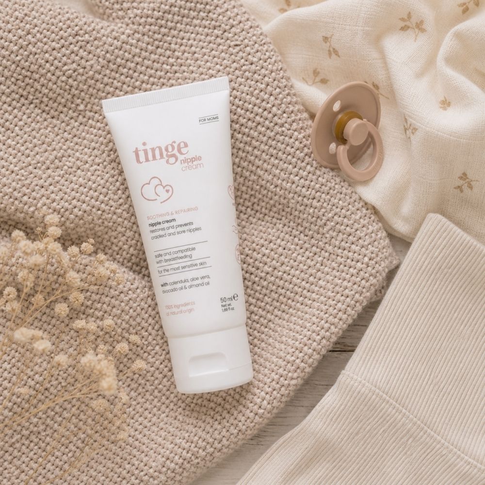 Crèmetube op een deken met fopspeen en kleding. Productnaam en opschrift: nipple cream.