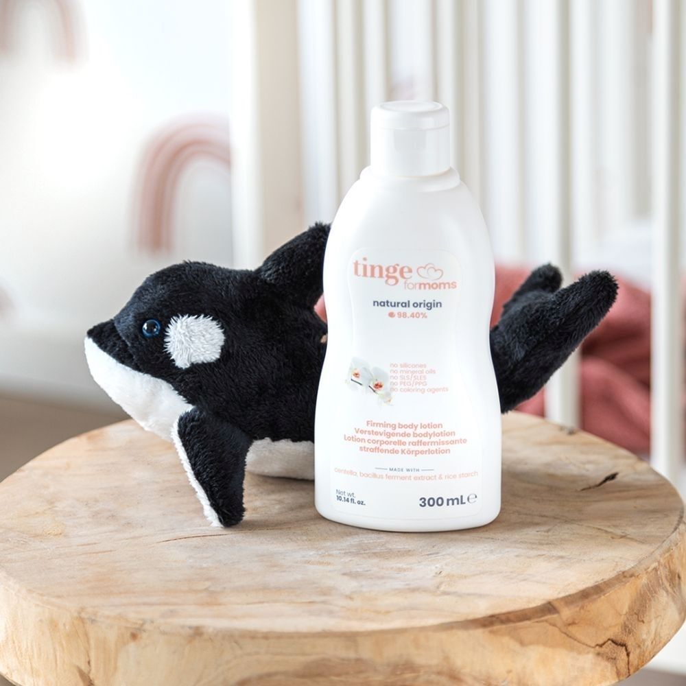 Fles bodylotion naast een orka knuffel op een houten tafel.