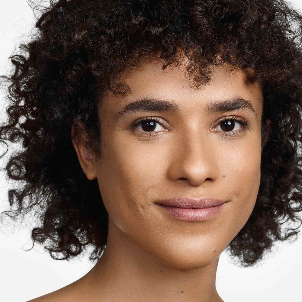 Portret van een vrouw met donker, krullend haar en een lichte huid. Ze draagt lichte make-up.
