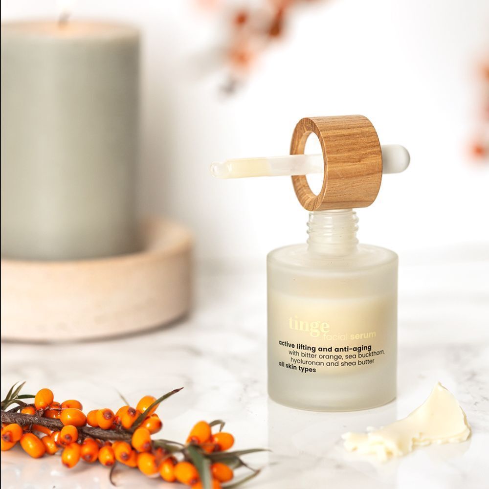 Flacon de sérum visage Tinge avec pipette sur table en marbre, près de bougie et baies.