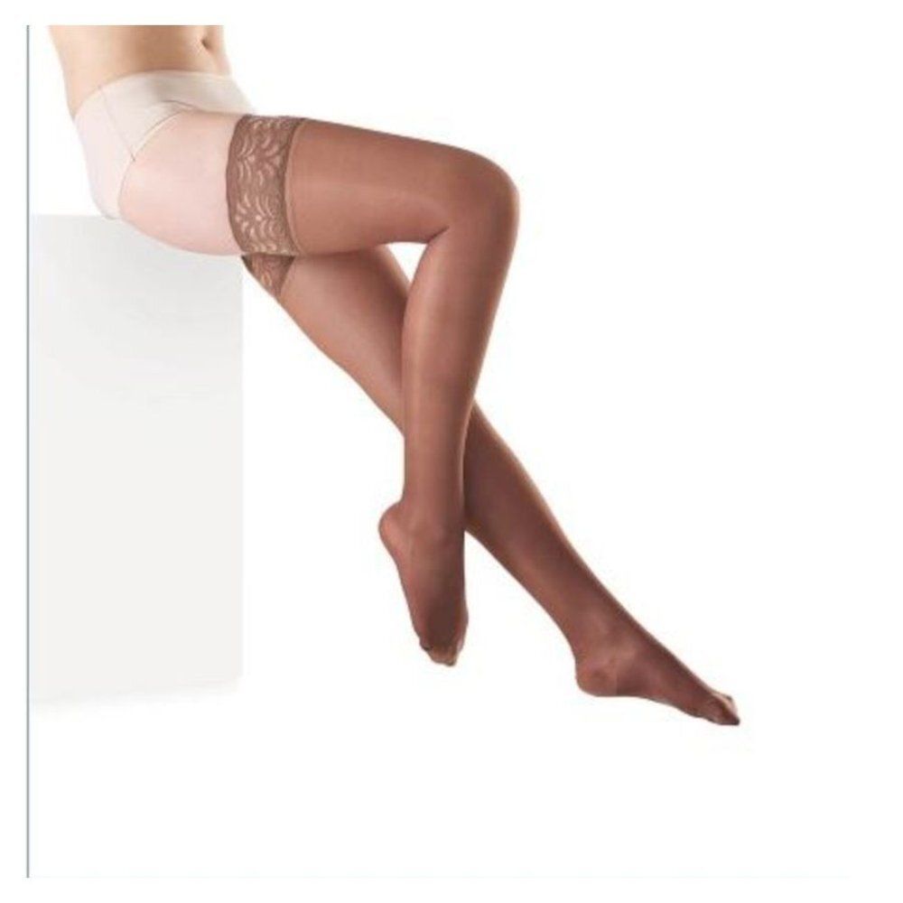 Bas autofixants couleur chair avec bande en dentelle marron sur la cuisse. Jambes croisées, sur fond blanc.