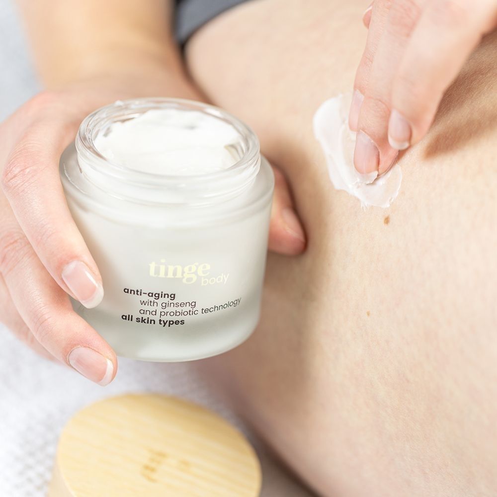 Een hand brengt Tinge Bodylotion Anti-Aging aan op de huid.
