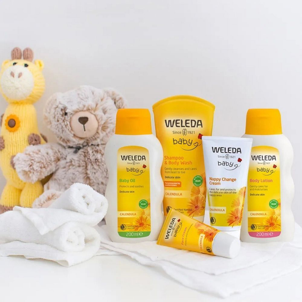 Divers produits Weleda Baby sur une surface blanche. Flacons, tubes et un ours en peluche. Design jaune et blanc.