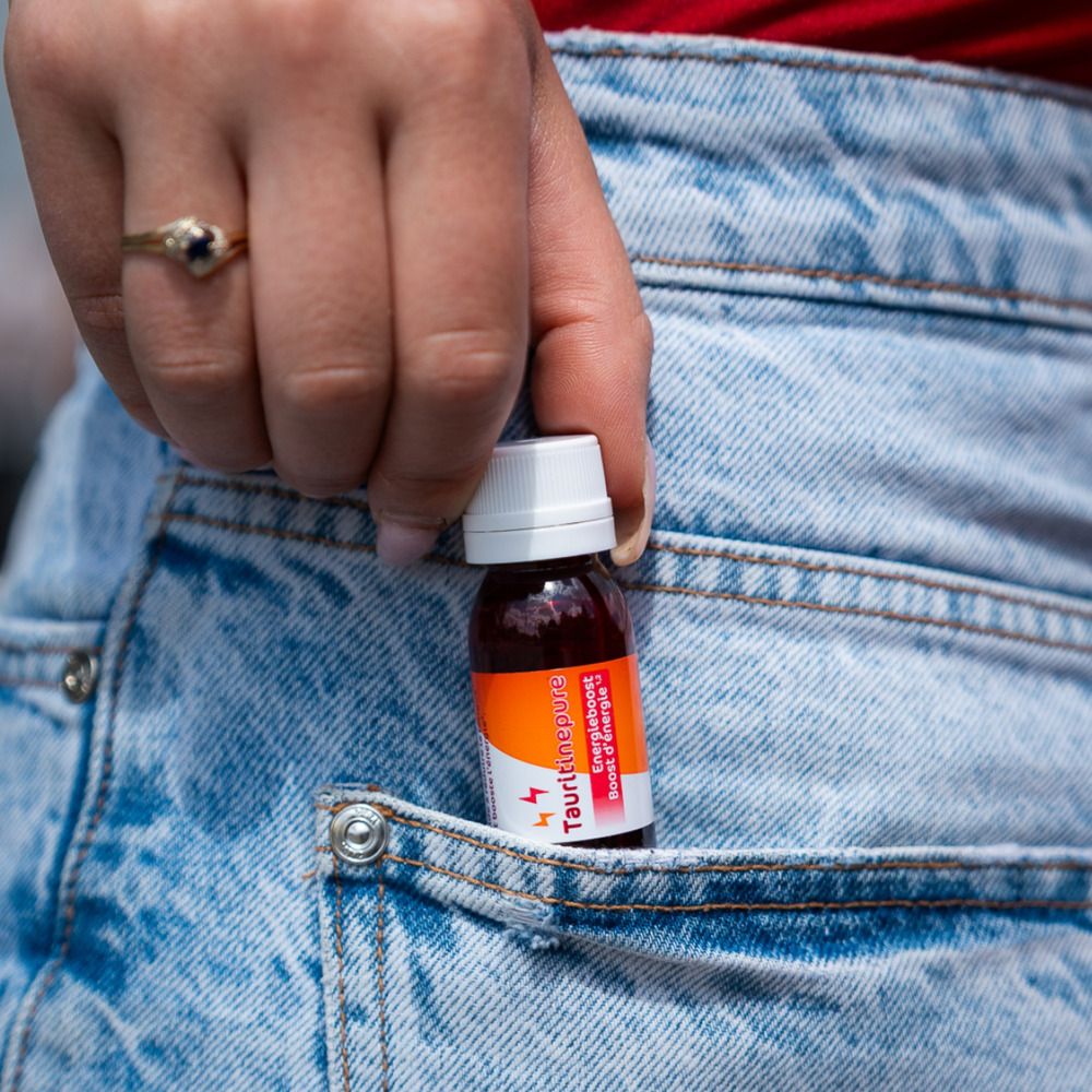 Hand met flesje TAURITINEPURE in jeanszak. Flesje met rode vloeistof.