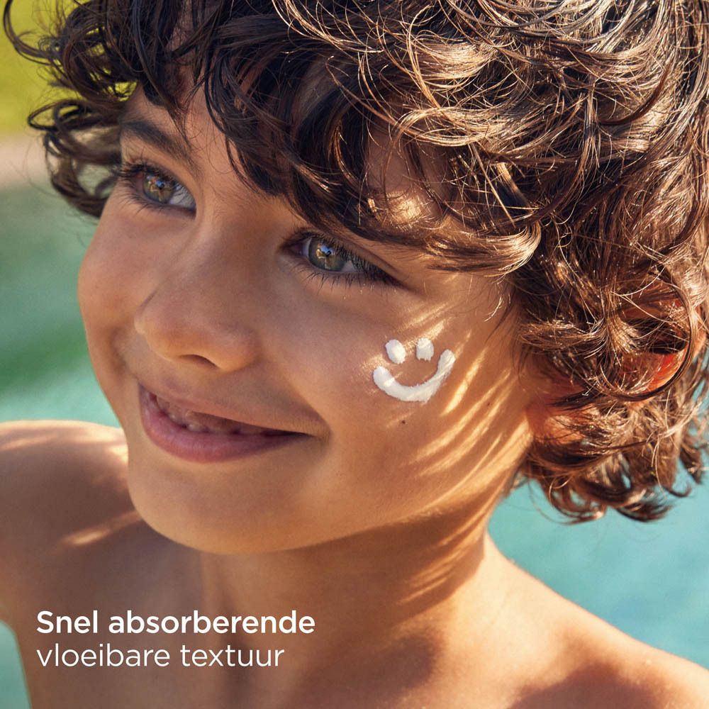 Enfant avec un smiley de crème solaire sur la joue. Texte: Snel absorberende vloeibare textuur.