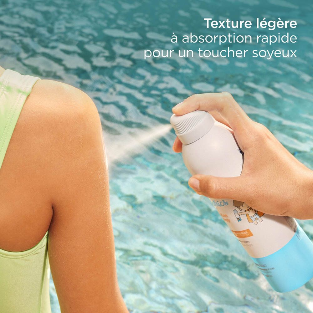 Personne vaporisant ISDIN Fotoprotector Pädiatrie Transparent Spray Wet Skin SPF50+ sur le bras. Eau en arrière-plan.