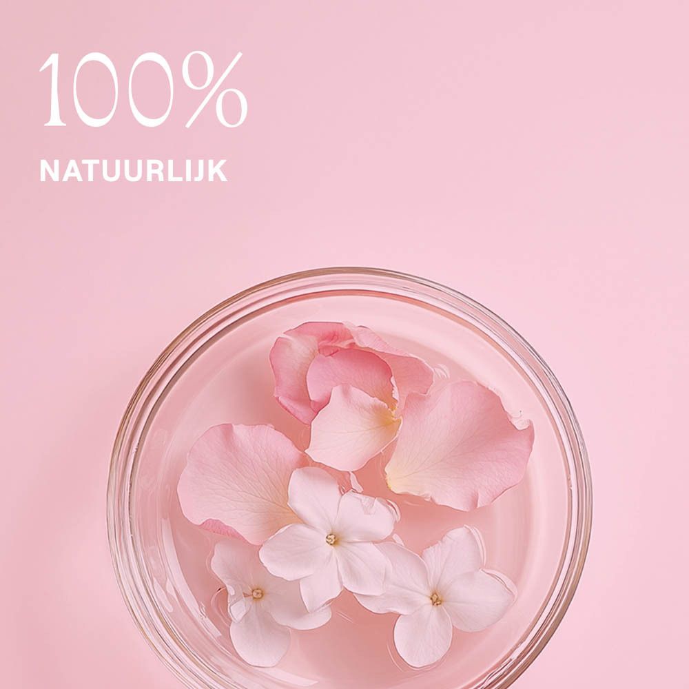Bloemblaadjes en bloemen in een glazen kom. Roze achtergrond. Tekst: 100% natuurlijk.
