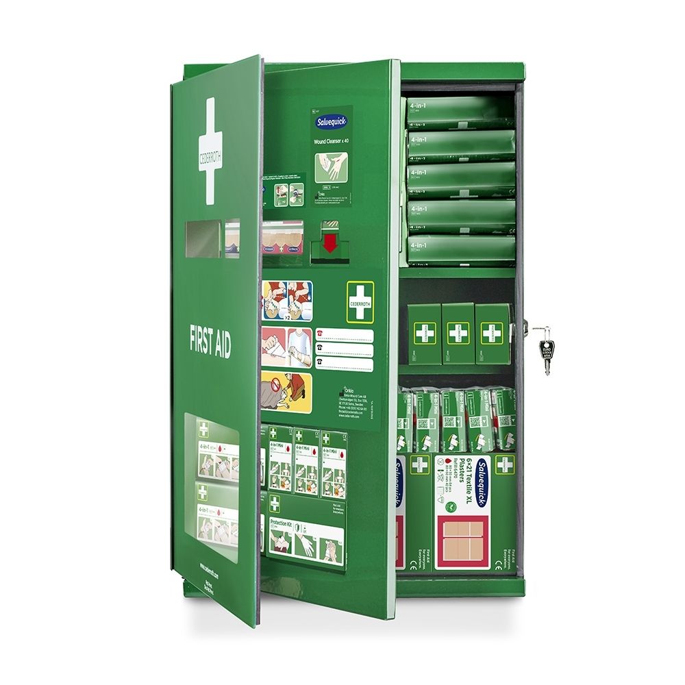 Armoire verte de premiers secours ouverte, étagères remplies et matériel de premiers secours visible.