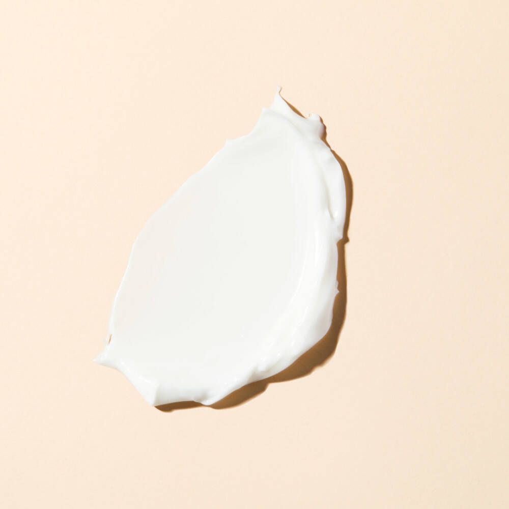 Klodder crème op beige achtergrond. Witte crème, glad en gestructureerd.