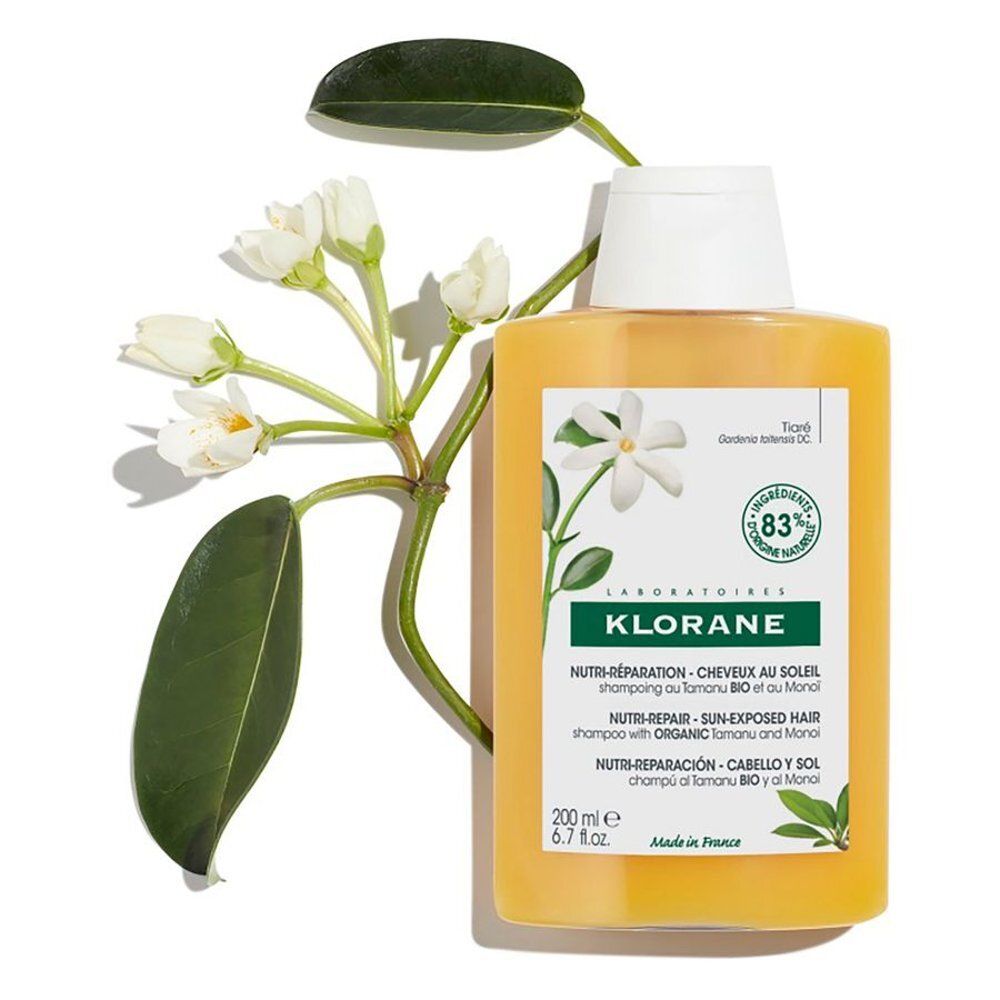 Geelachtige shampoo fles met witte dop. Opschrift Klorane, Nutri-Réparation, Cheveux Soleil, Shampooing au Tamanu Bio et au Monoï. 83% ingrediënten van natuurlijke oorsprong.