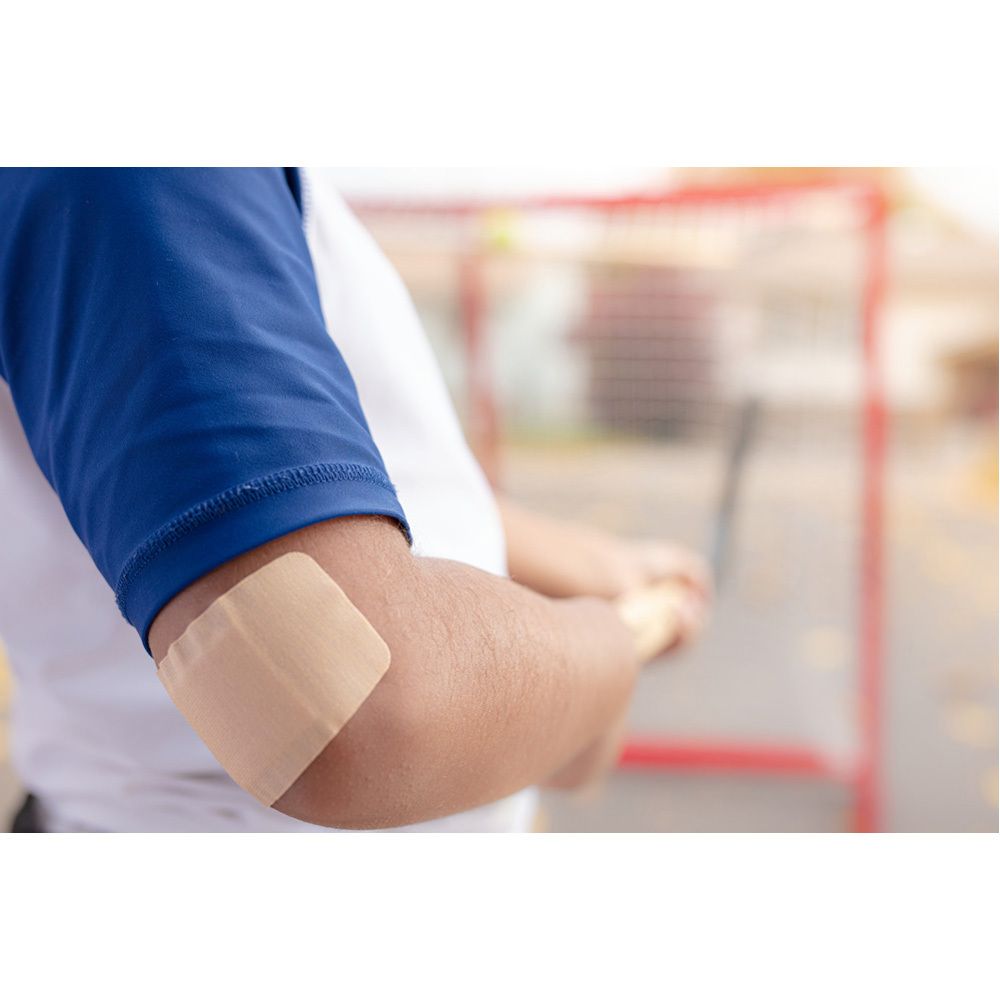 Persoon met Nexcare Duo pleister op de elleboog. Beige.