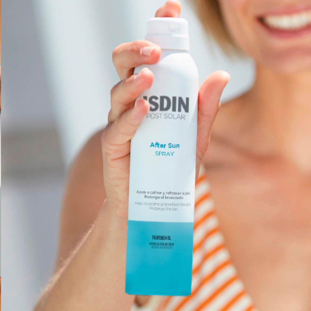 Personne tenant un flacon spray blanc et bleu. Inscription: ISDIN POST SOLAR After Sun SPRAY. Application sur la peau.